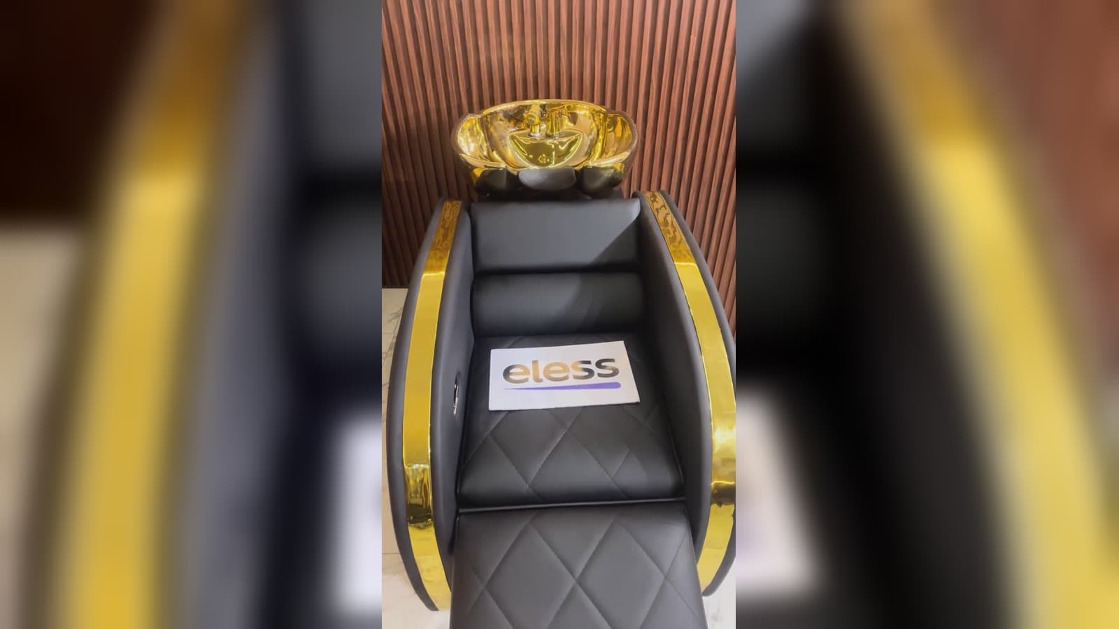 Lavacabeza dorado con sillón negro capitoné y panel de madera en el showroom de ELESS